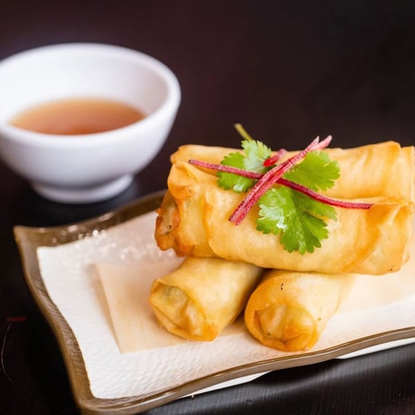 Crispy golden spring rolls garnished with cilantro and red radish, served with a dipping sauce.