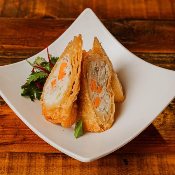 Two crispy fried spring rolls, one cut in half, revealing a filling of meat and vegetables.
